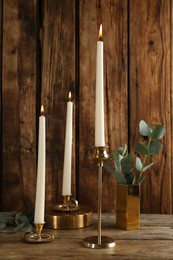 Photo of Elegant candlesticks with burning candles and eucalyptus on wooden table