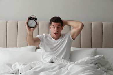 Photo of Emotional man with alarm clock in bed. Being late because of oversleeping