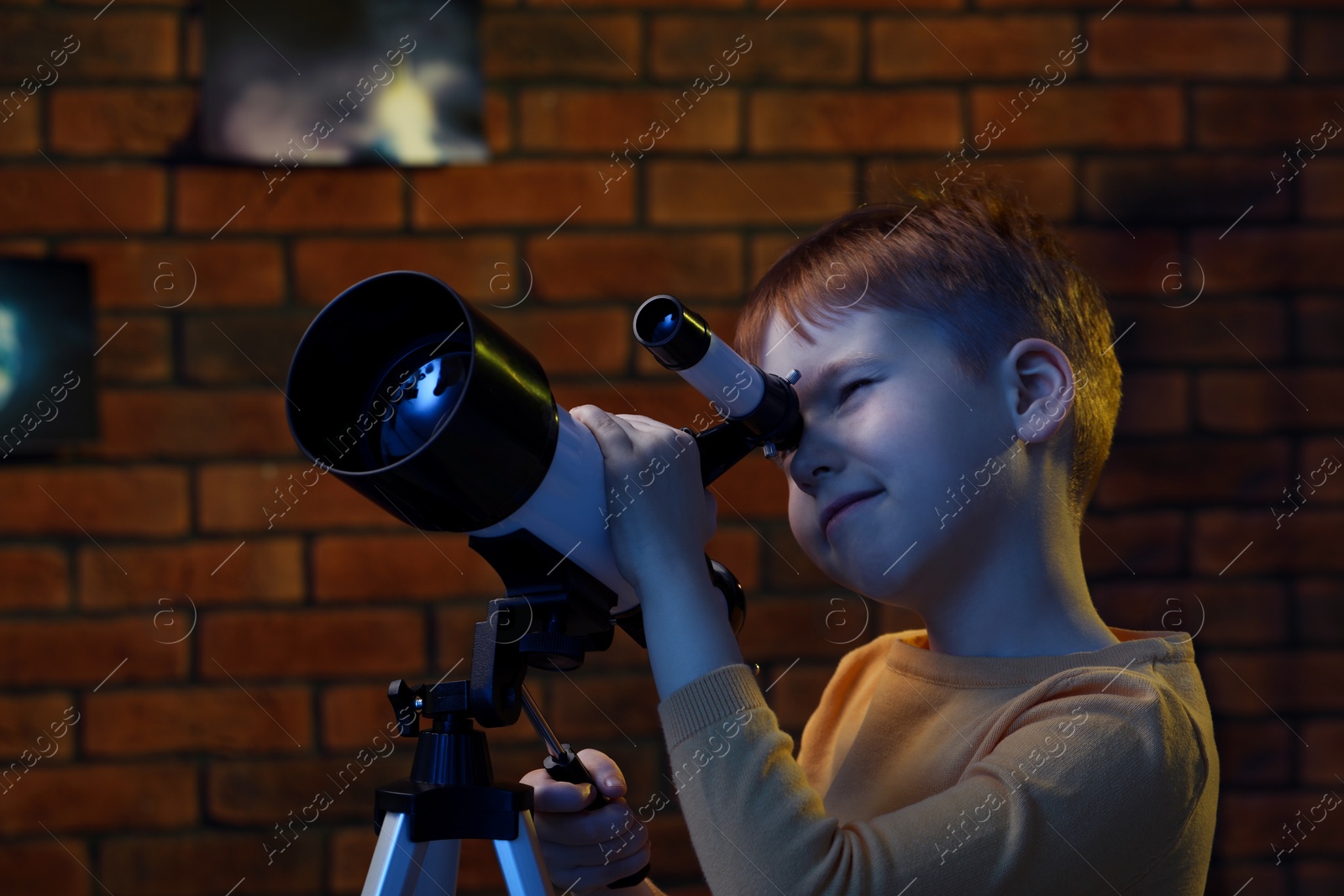 Photo of Little boy looking at stars through telescope in room