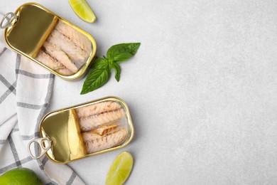 Open tin cans with mackerel fillets, lime and basil on grey table, flat lay. Space for text