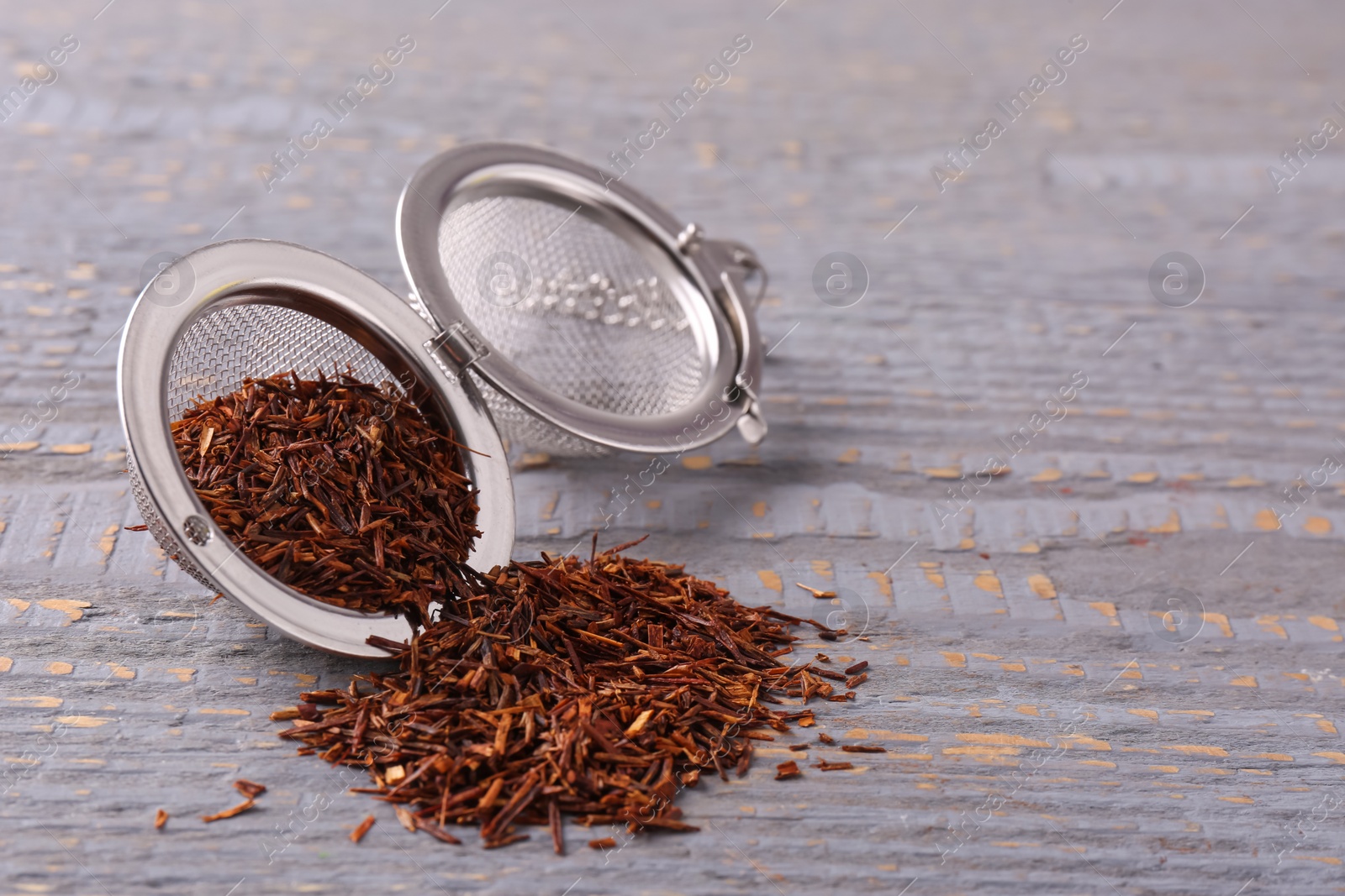Photo of Infuser with dry rooibos leaves on grey wooden table, space for text