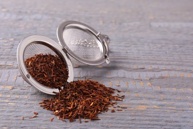 Photo of Infuser with dry rooibos leaves on grey wooden table, space for text