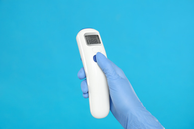 Photo of Doctor holding non contact infrared thermometer on light blue background, closeup. Measuring temperature