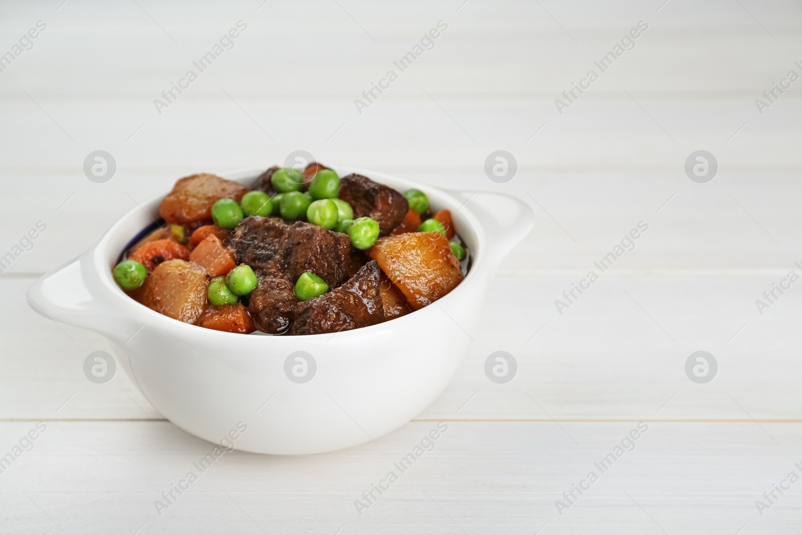 Photo of Delicious beef stew with carrots, peas and potatoes on white wooden table, closeup. Space for text