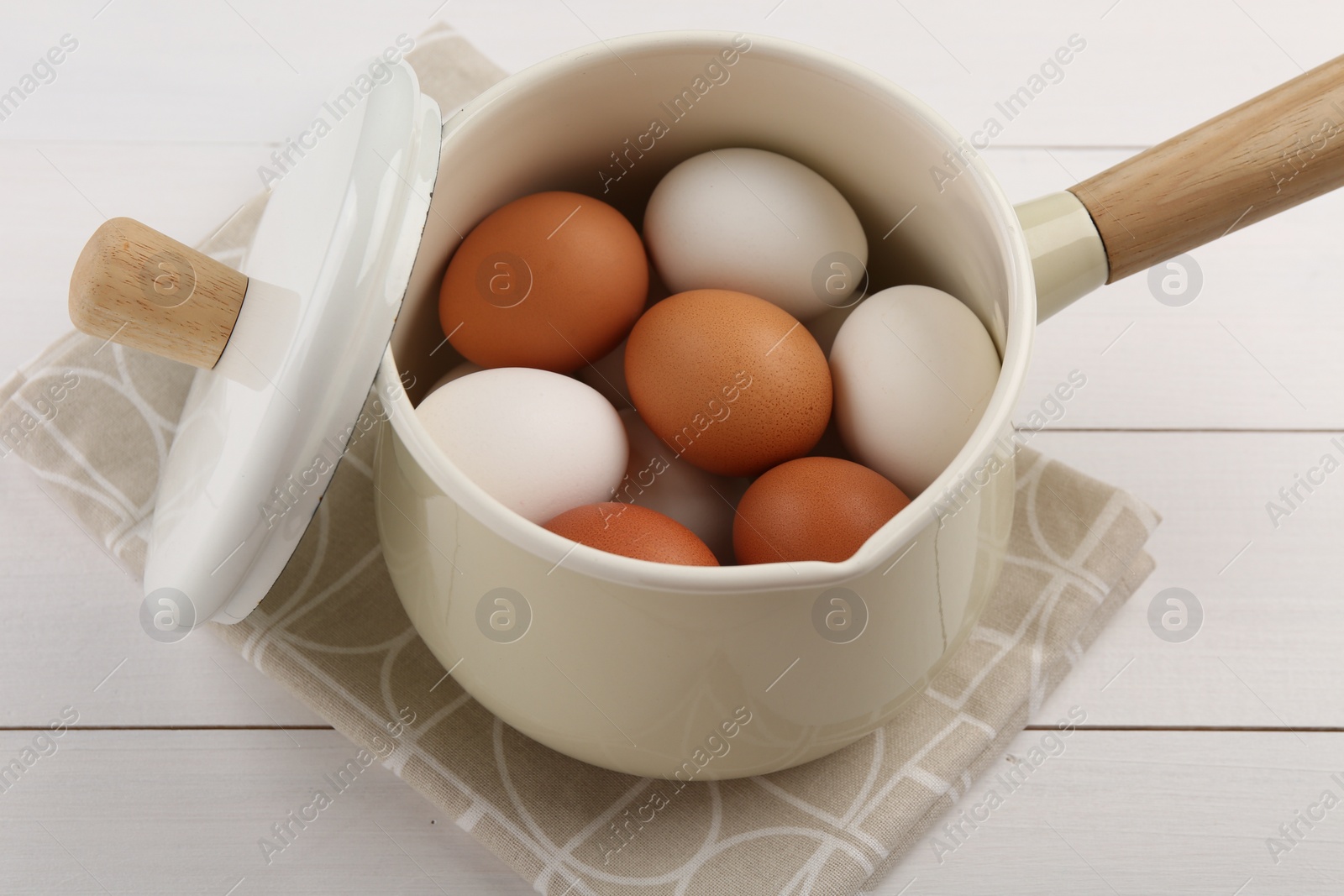 Photo of Unpeeled boiled eggs in pan on white wooden table, closeup