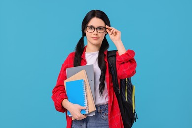 Student with notebooks, folder and backpack on light blue background