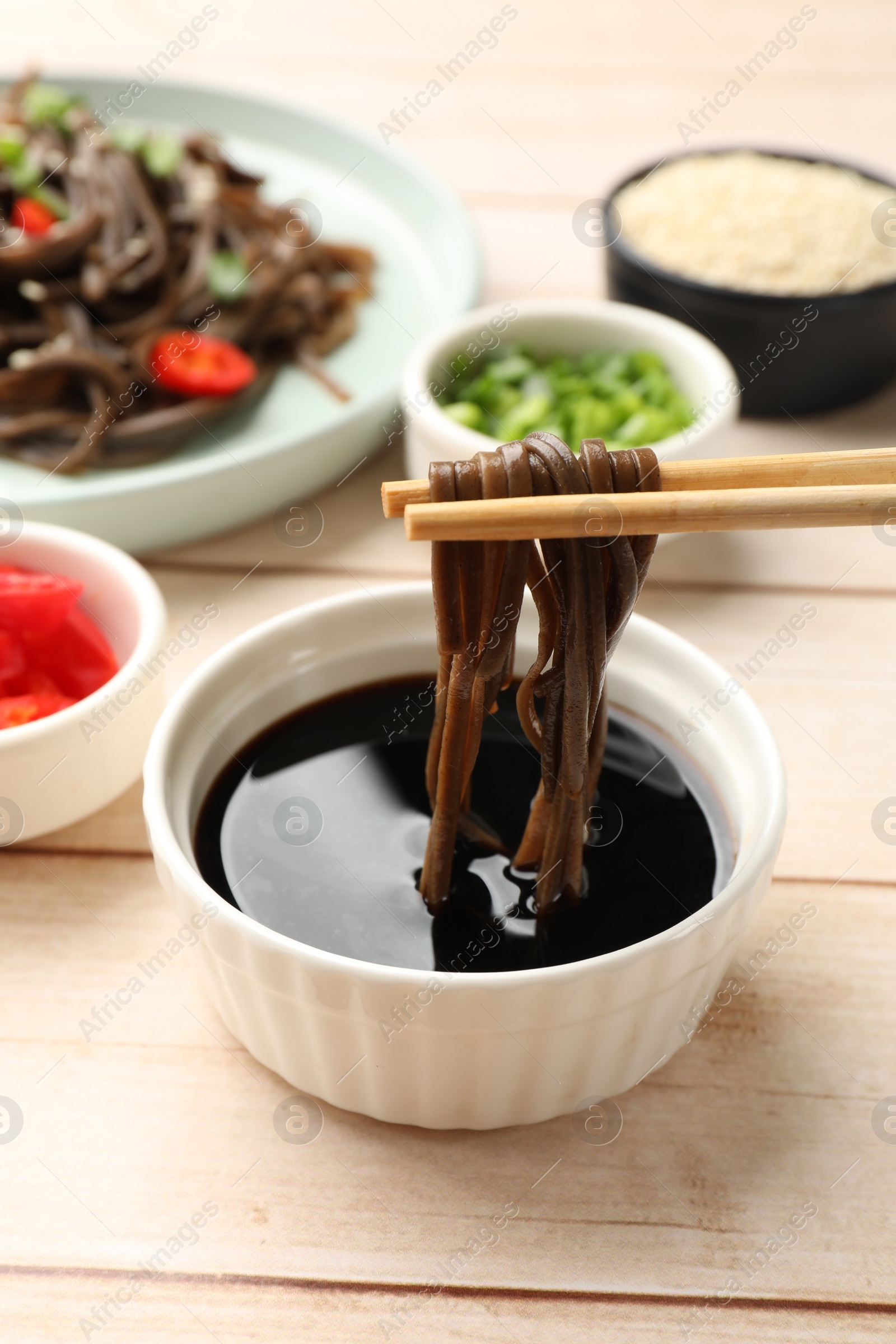 Photo of Eating delicious buckwheat noodles (soba) with chopsticks at white wooden table, closeup