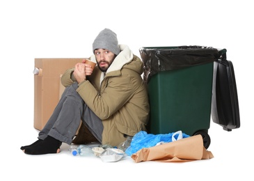 Poor homeless man sitting near trash bin isolated on white
