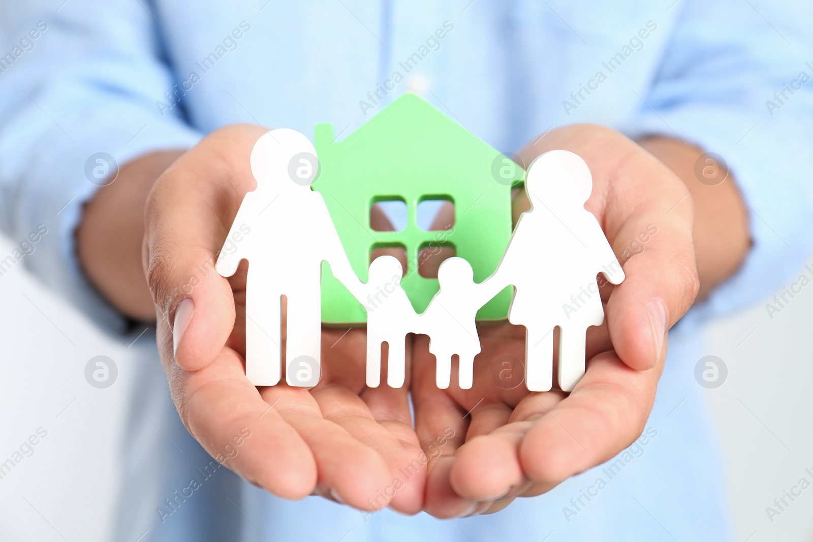 Photo of Young man holding wooden family figure and house model, closeup of hands