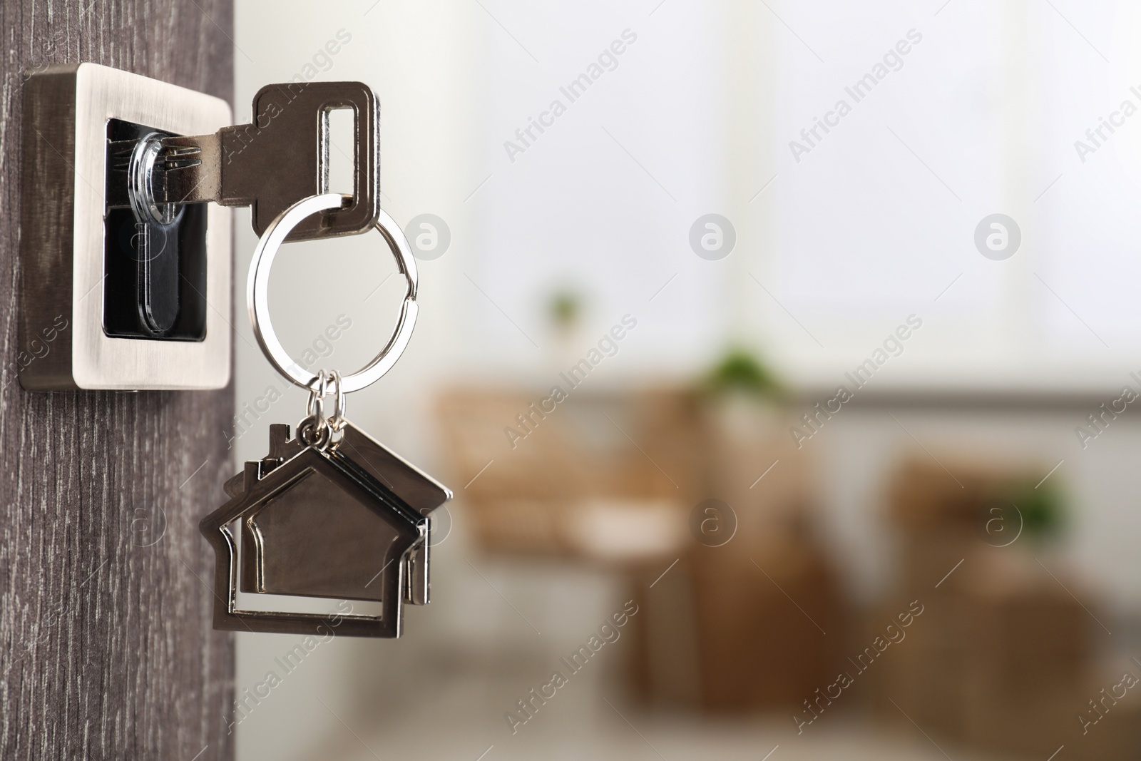 Photo of Mortgage and real estate. Open door with key and house shaped keychain against blurred background, space for text