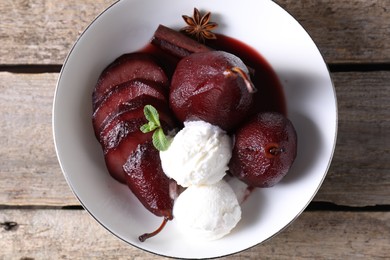 Tasty red wine poached pears and ice cream in bowl on wooden table, top view