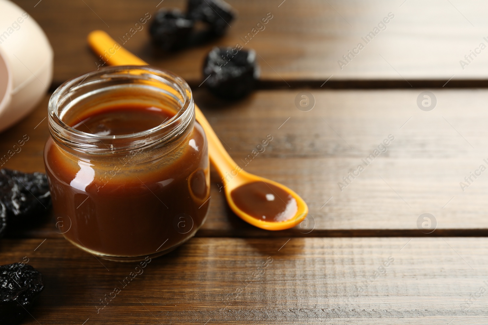 Photo of Tasty baby food in jar, spoon and dried prunes on wooden table, space for text