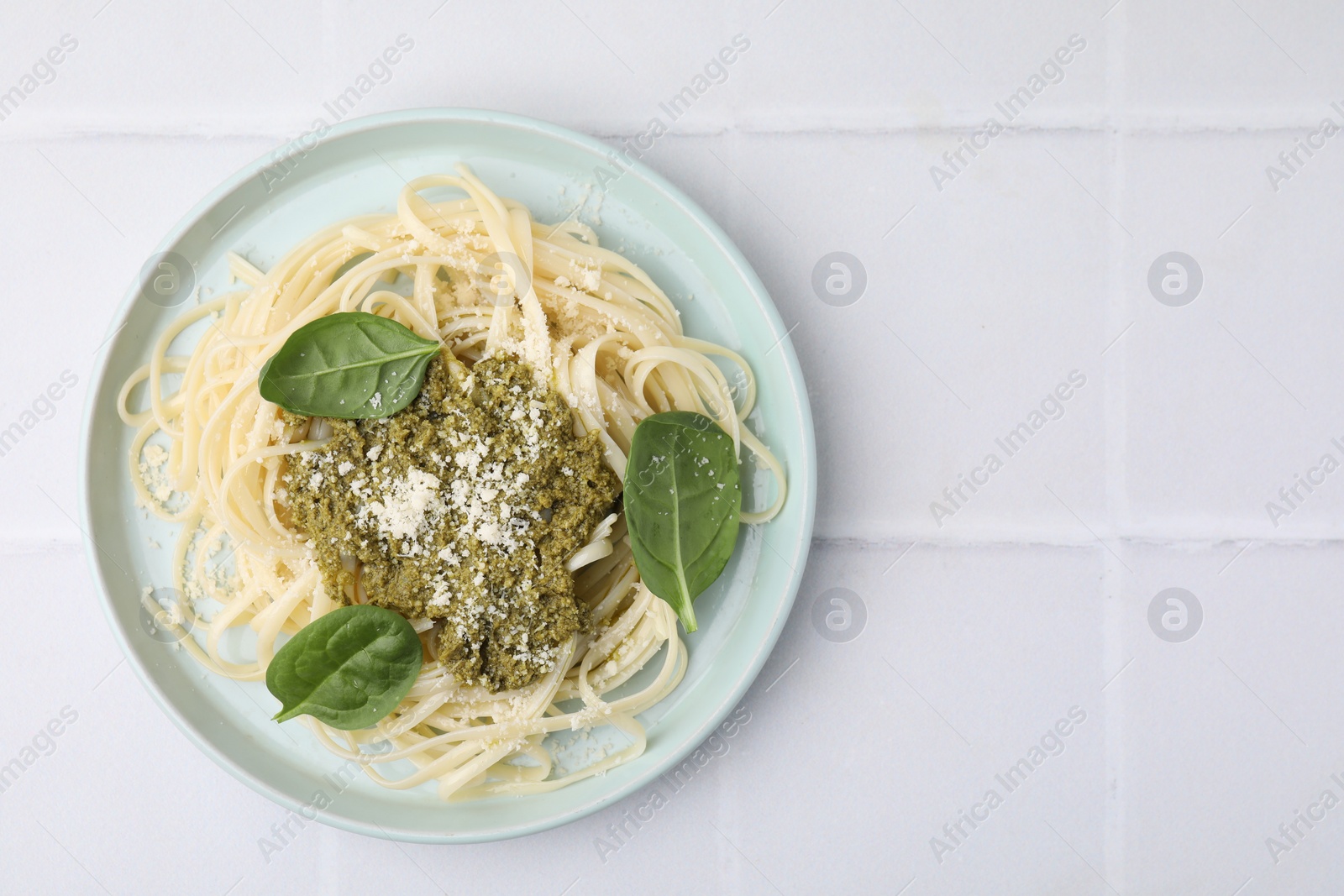 Photo of Tasty pasta with spinach, cheese and sauce on white tiled table, top view. Space for text