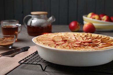 Tasty apple pie in baking dish on grey table