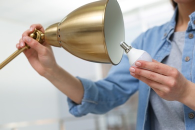 Woman changing light bulb in lamp indoors, closeup