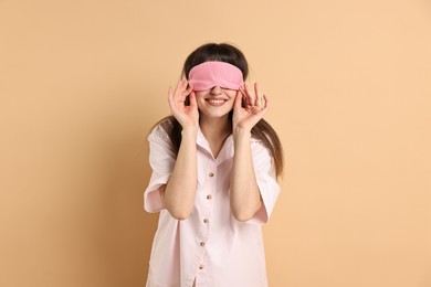 Woman in pyjama and sleep mask on beige background