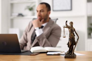 Photo of Lawyer working with laptop at table in office, focus on statue of Lady Justice