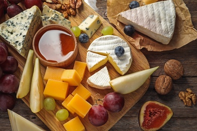 Photo of Board with different kinds of delicious cheese and snacks on wooden background, above view