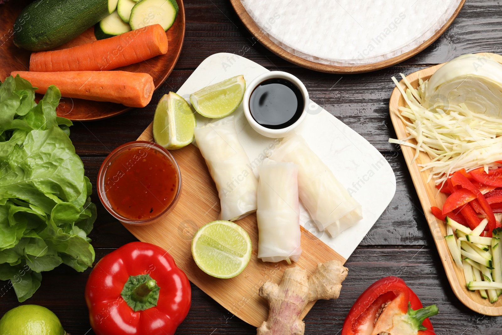 Photo of Delicious spring rolls with vegetables, lime and sauces on wooden table, flat lay