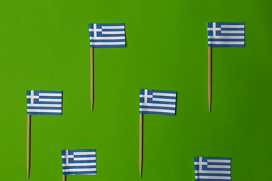 Photo of Small paper flags of Greece on green background, flat lay