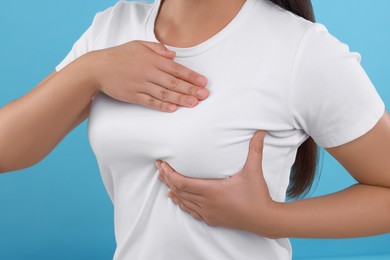 Photo of Woman doing breast self-examination on light blue background, closeup