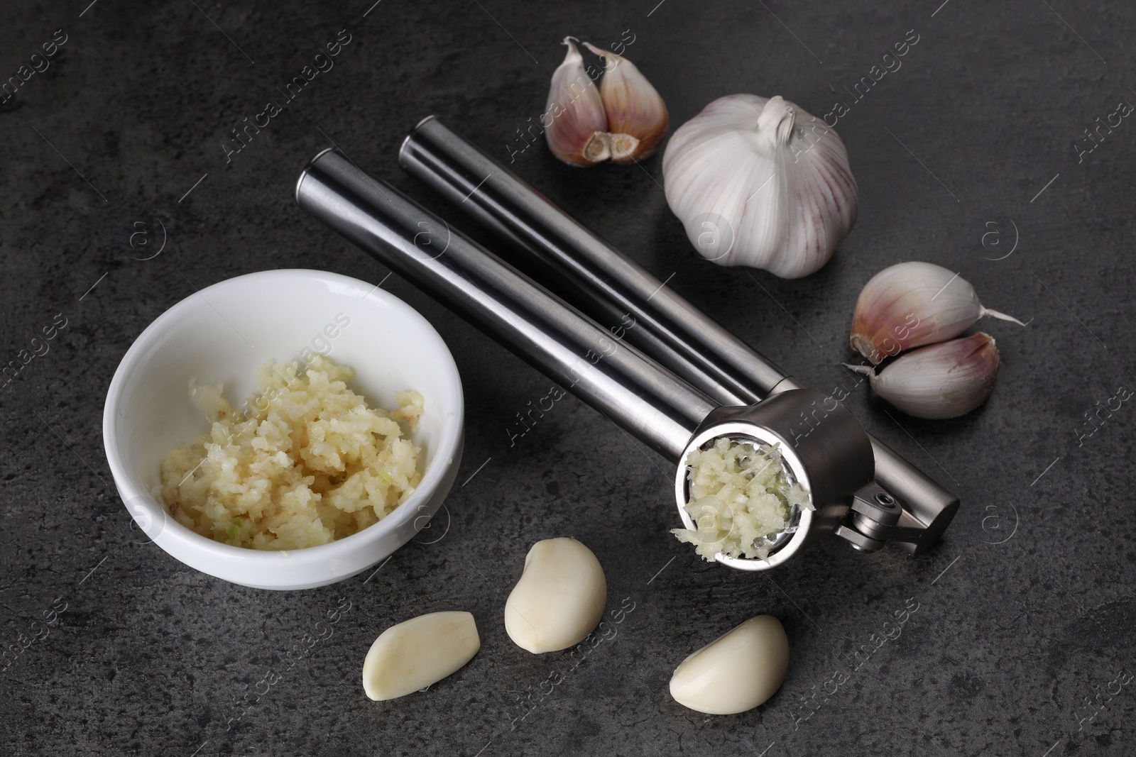 Photo of Garlic press, cloves and mince on grey table. Kitchen utensil