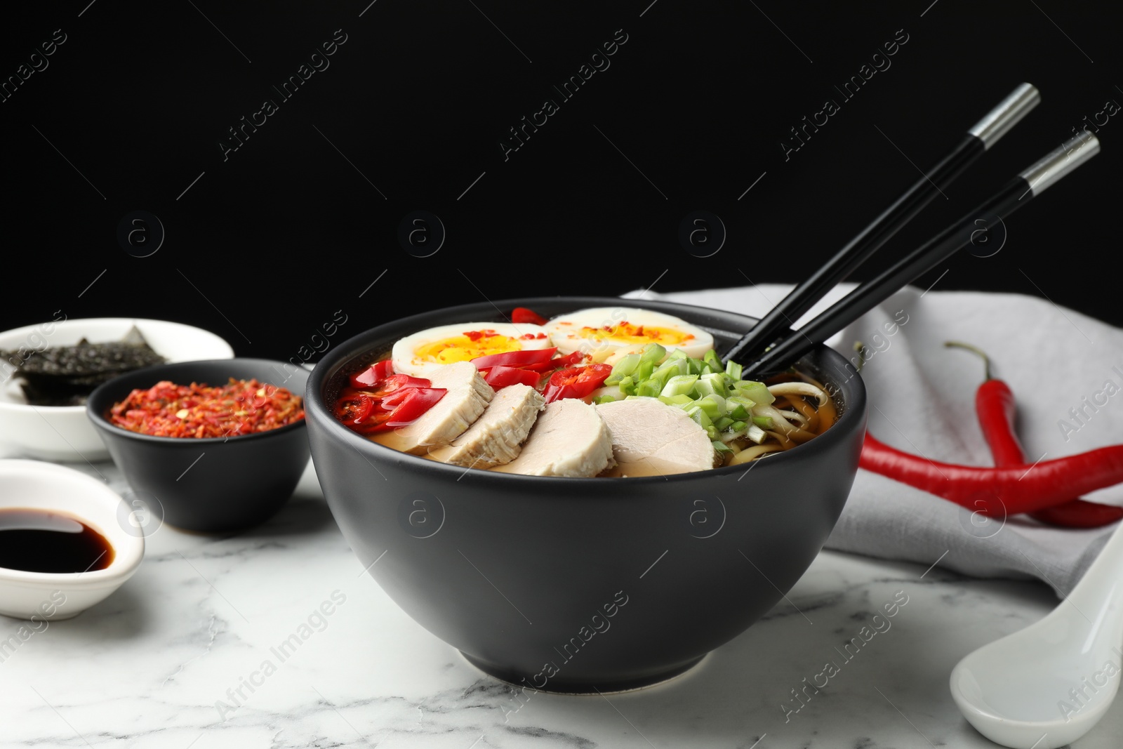 Photo of Delicious ramen in bowl on white marble table against black background, closeup. Noodle soup