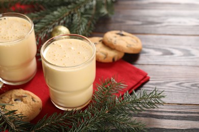 Photo of Tasty eggnog, cookies and fir branches on wooden table. Space for text
