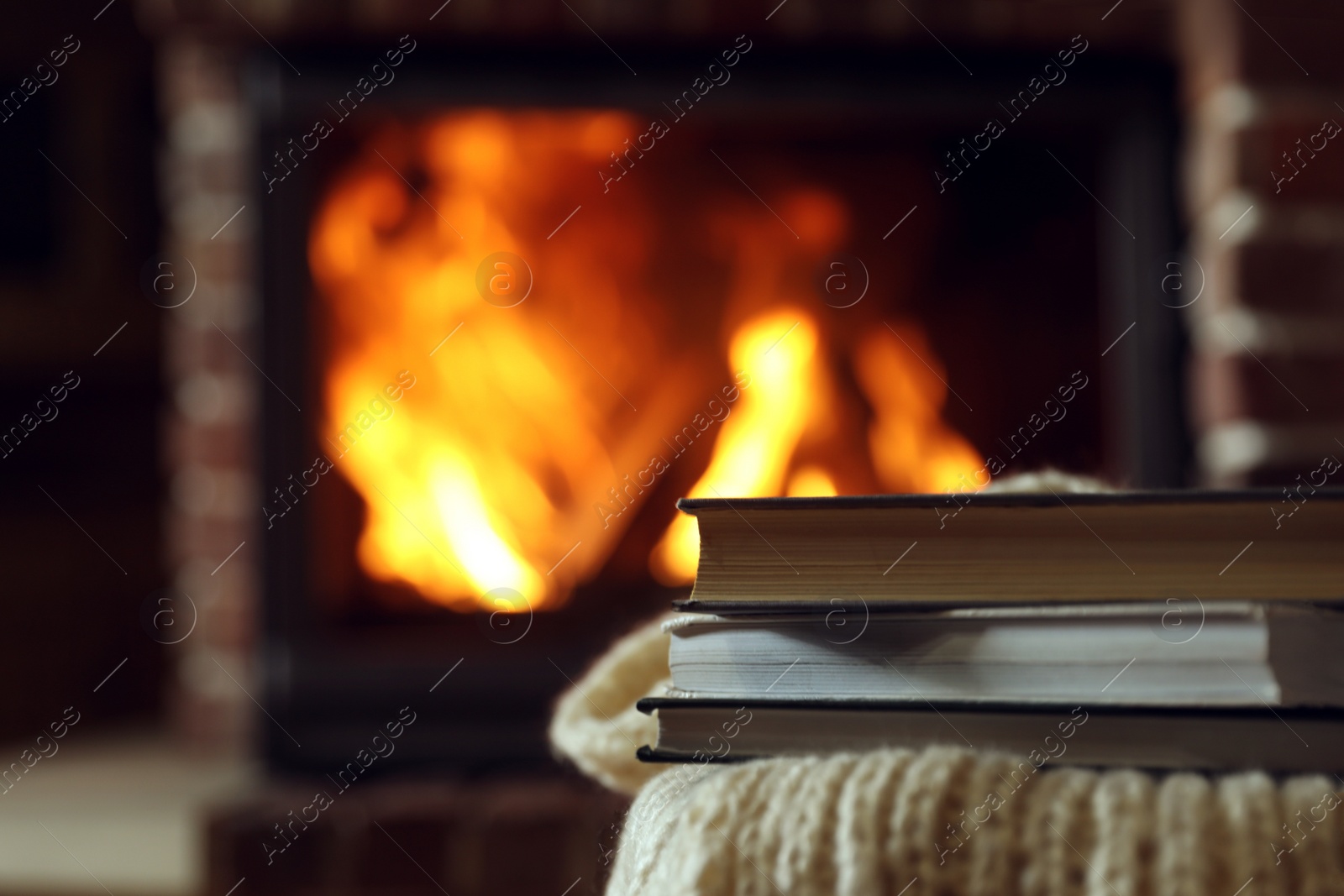 Photo of Books on table near burning fireplace, space for text. Reading at home