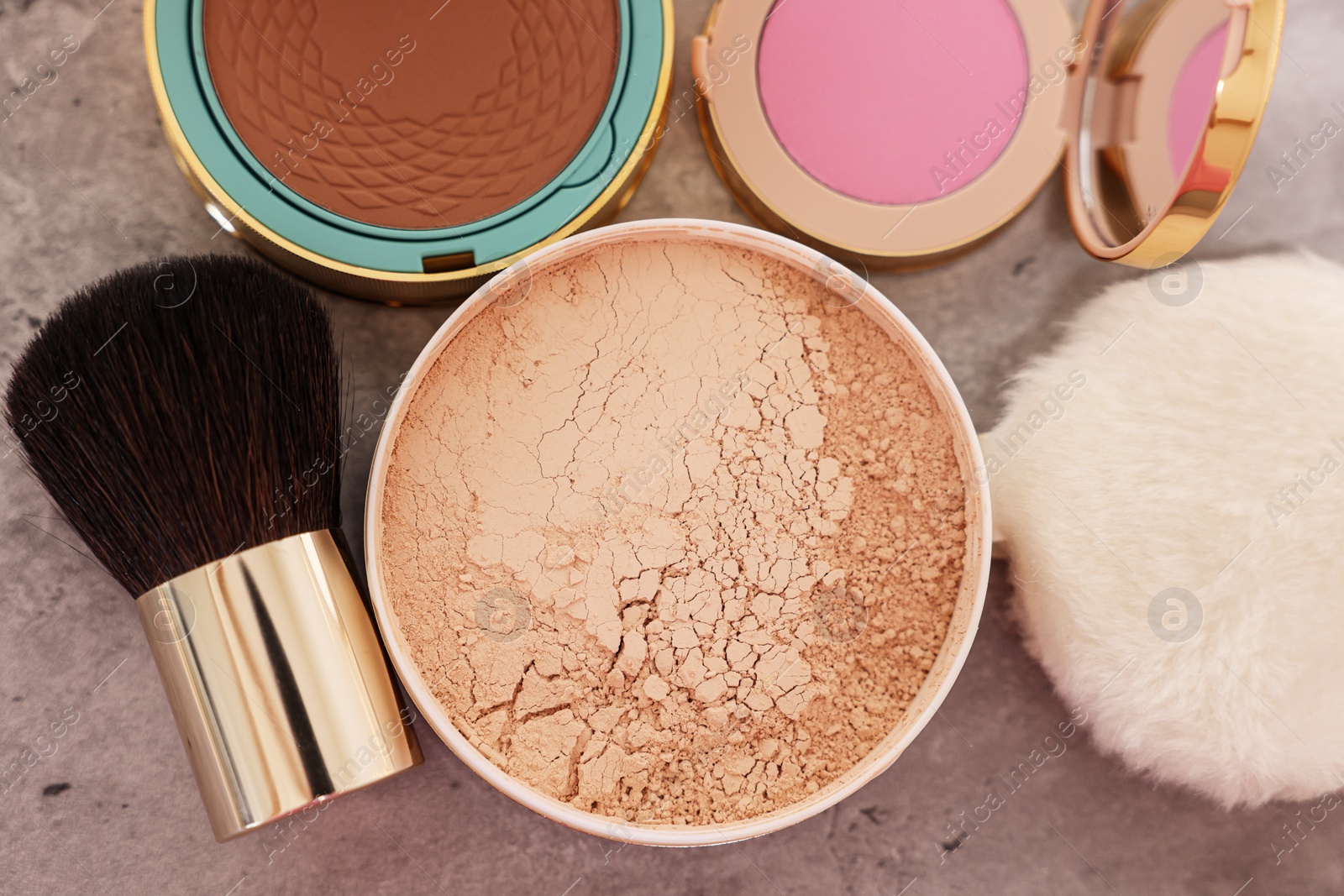 Photo of Bronzer, powder, blusher and brush on grey textured table, flat lay