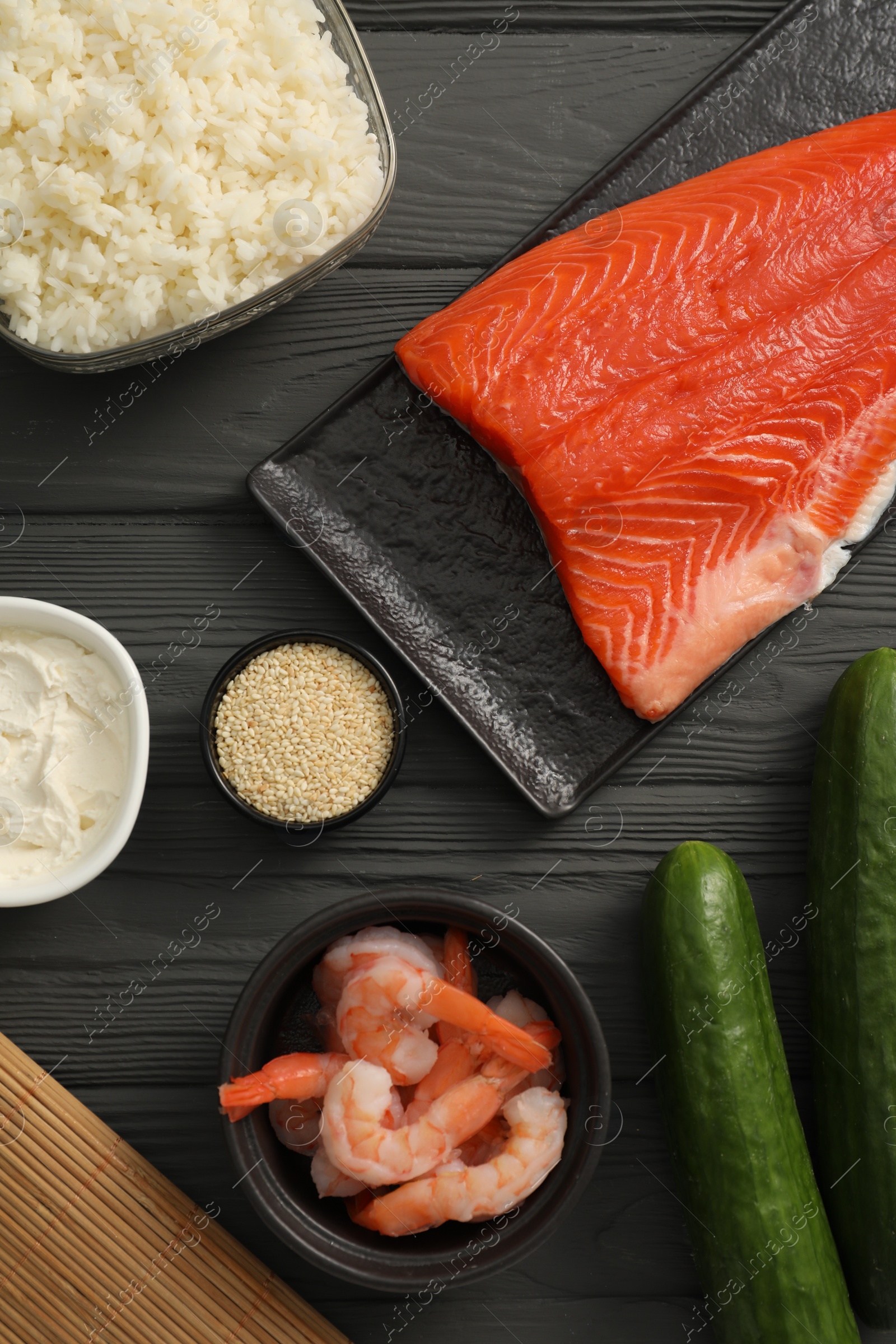 Photo of Making sushi rolls. Flat lay composition with ingredients on black wooden table