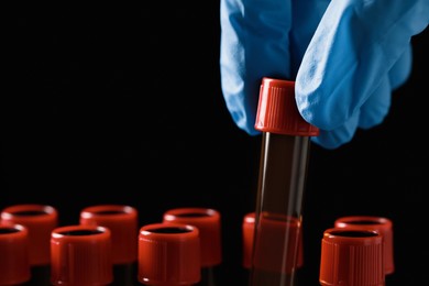 Photo of Scientist putting test tube with brown liquid into stand against black background, closeup
