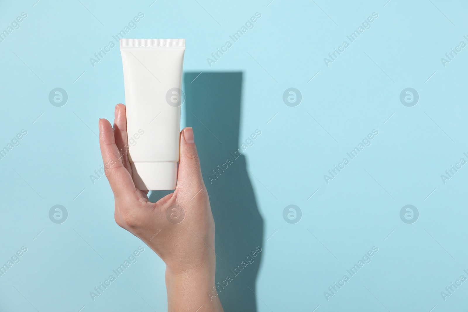 Photo of Woman with tube of hand cream on light blue background, top view. Space for text