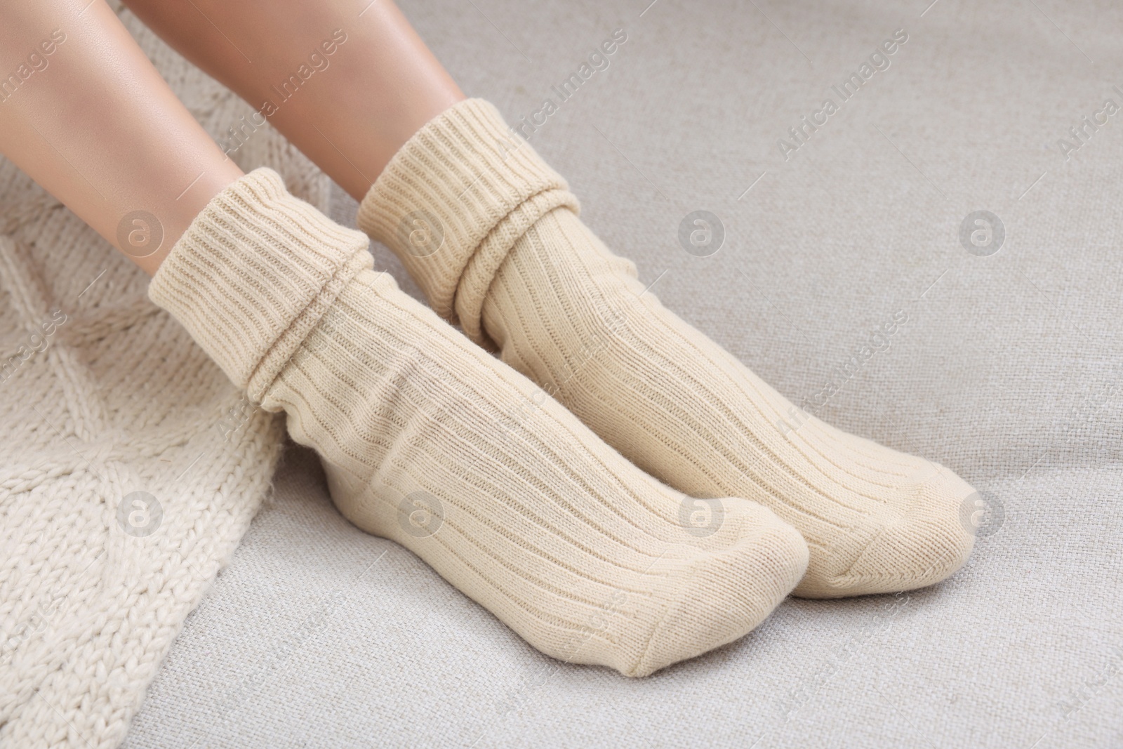 Photo of Woman in warm socks on sofa at home, closeup