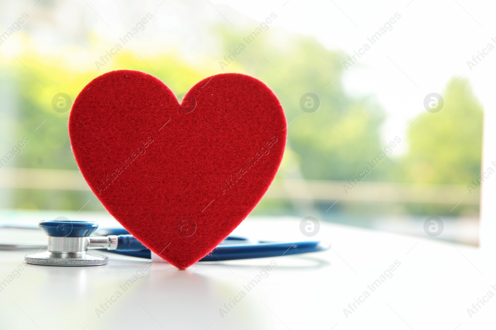 Photo of Red heart and stethoscope on table against blurred background