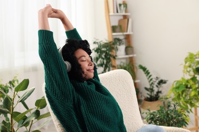 Photo of Woman wearing headphones and listening music in room with beautiful houseplants