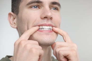 Photo of Young man applying whitening strip on his teeth against light grey background, closeup. Space for text