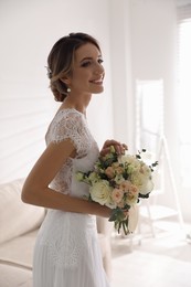 Beautiful young bride in wedding dress holding bouquet indoors