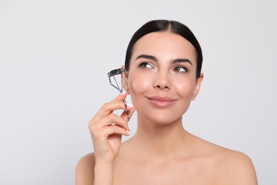 Beautiful young woman with eyelash curler on white background