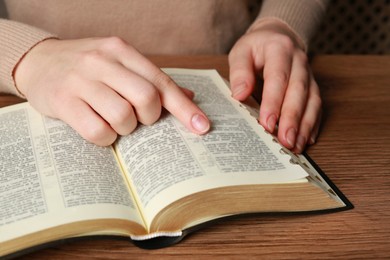 Photo of Woman reading Bible at wooden table, closeup