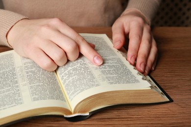 Woman reading Bible at wooden table, closeup