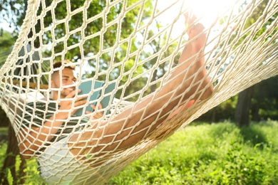 Photo of Young man reading book in comfortable hammock at green garden