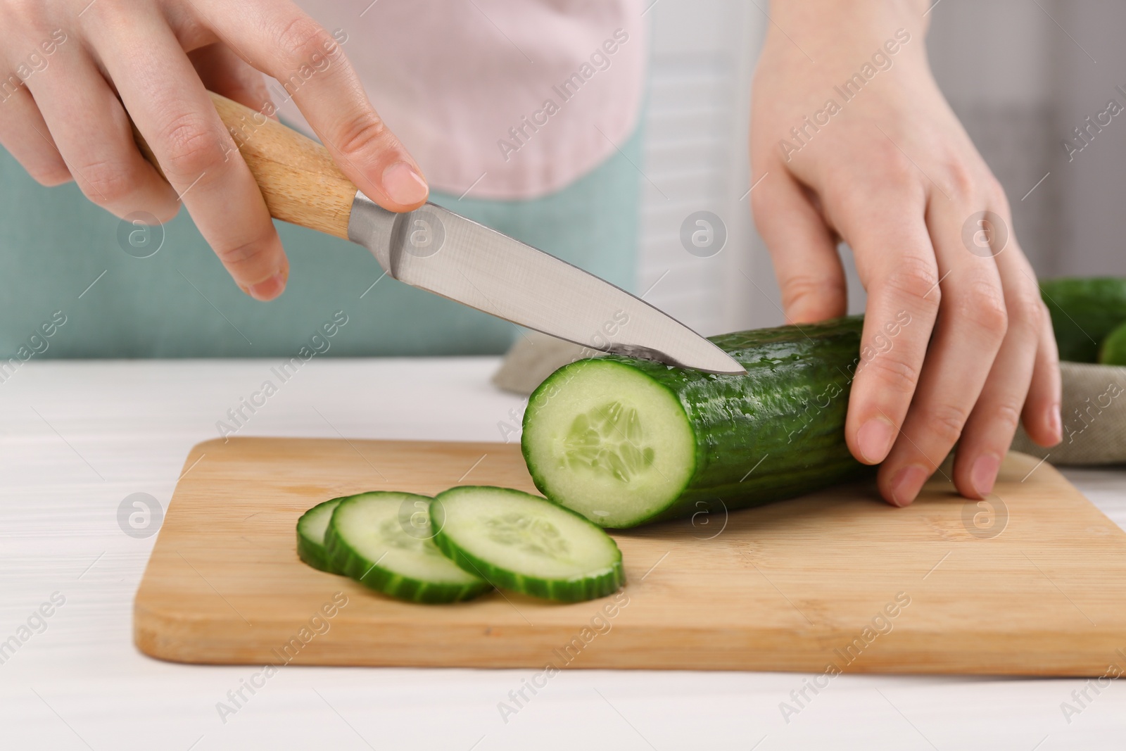 Photo of Woman cutting cucumber on wooden board at white table, closeup