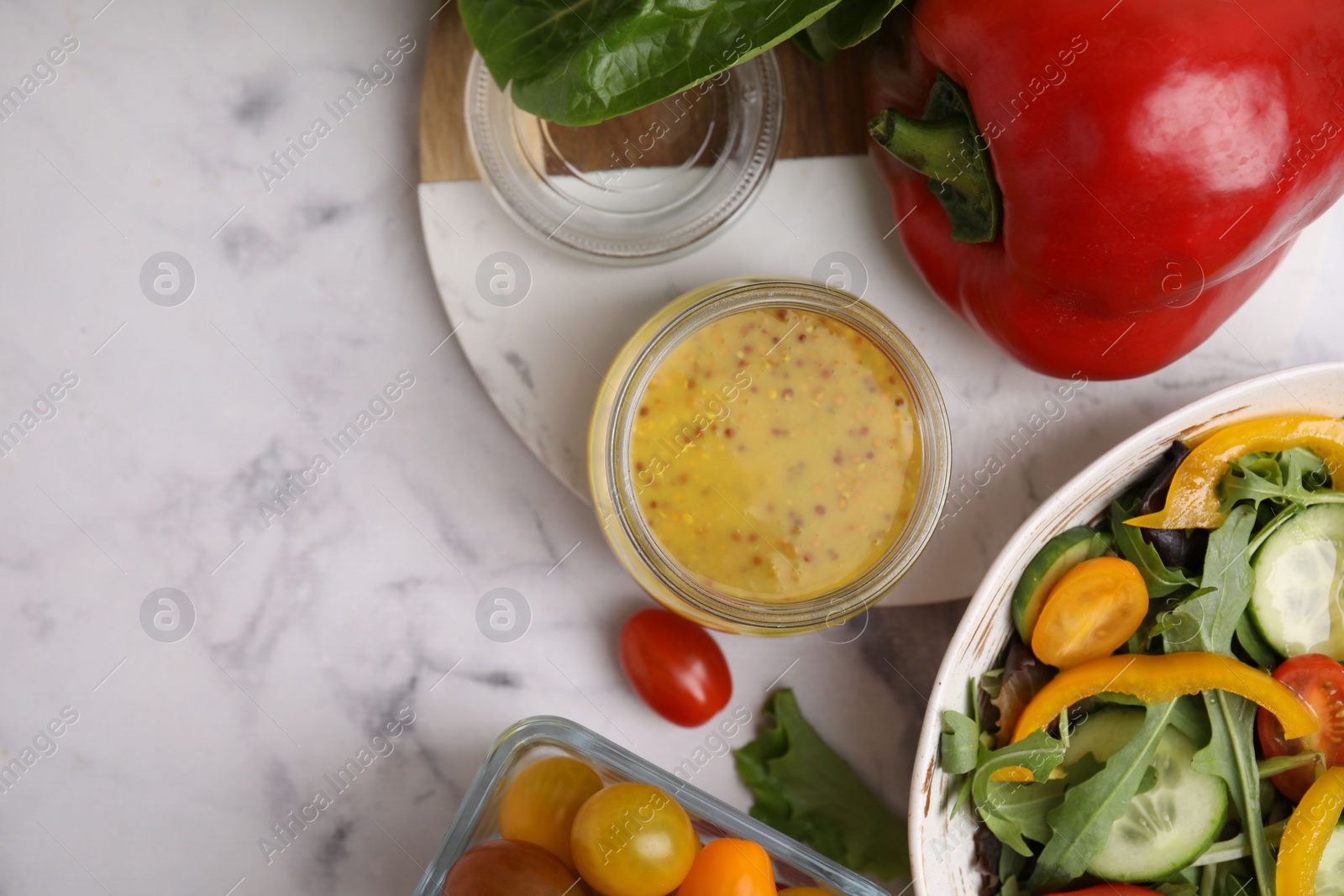 Photo of Tasty vinegar based sauce (Vinaigrette) in jar, salad and products on white marble table, flat lay. Space for text