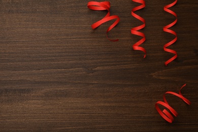 Red serpentine streamers on wooden table, flat lay. Space for text