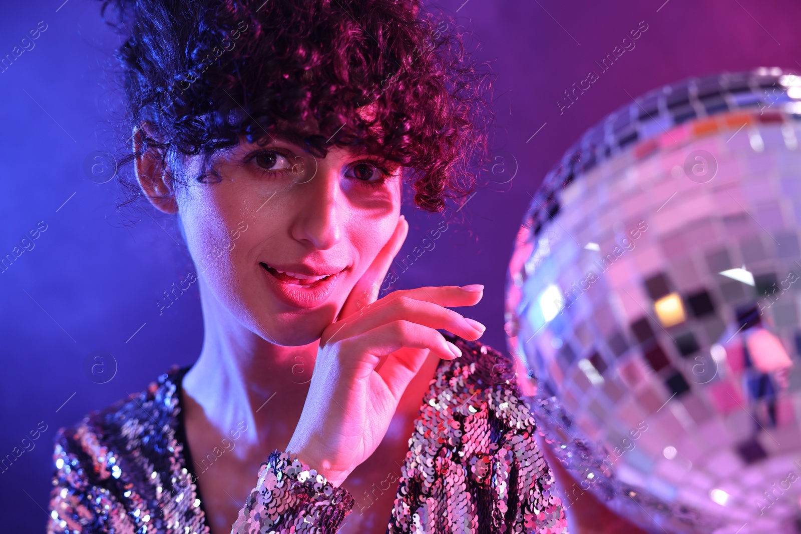Photo of Beautiful young woman with disco ball posing on color background in neon lights
