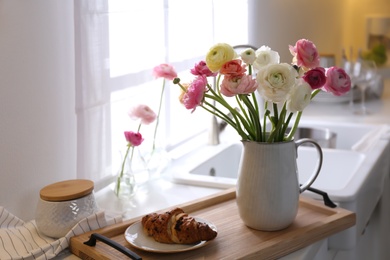 Photo of Wooden tray with beautiful ranunculus flowers and fresh croissant in kitchen