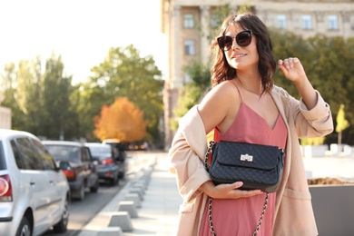 Photo of Young woman in sunglasses with stylish black bag on city street