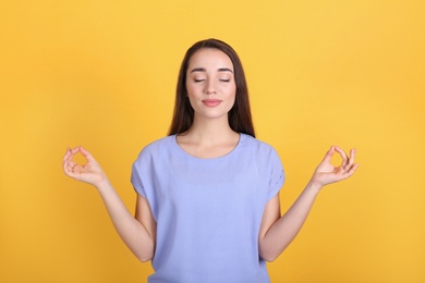 Young woman meditating on yellow background. Stress relief exercise