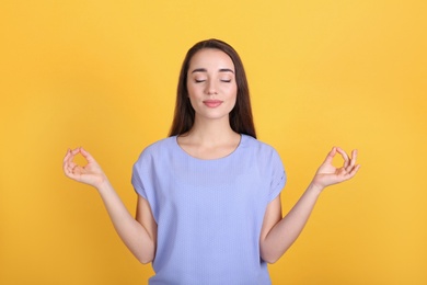 Photo of Young woman meditating on yellow background. Stress relief exercise